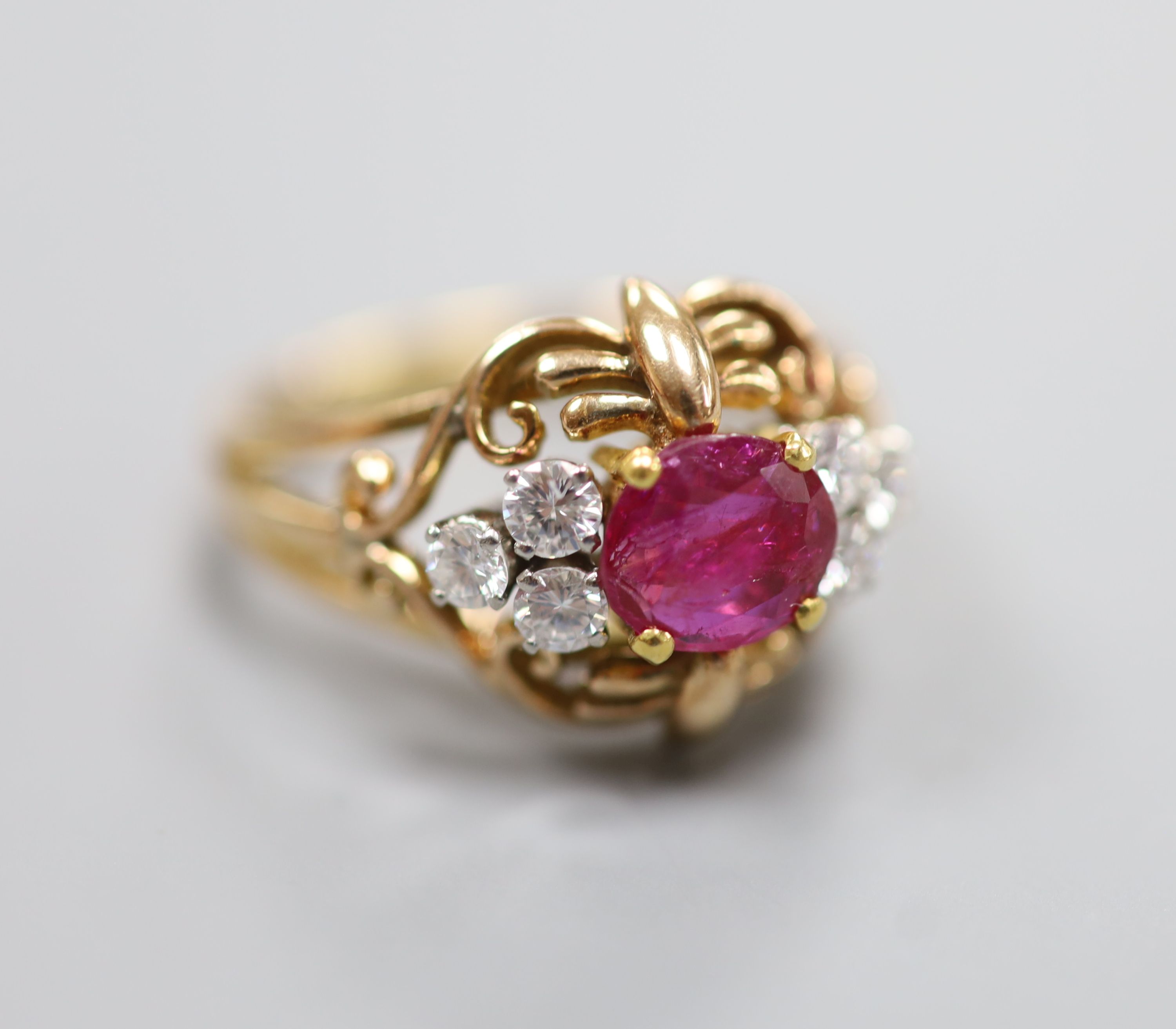 A stylish yellow metal, ruby and diamond set cluster ring, with single round cut ruby(crack), flanked by six round cut diamonds, in an openwork scroll setting, size Q/R, gross weight 7.5 grams, in a Cartier box.